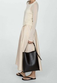 Bolso tote de cuero negro con una forma estructurada y una sola correa para el hombro, combinado con una blusa beige de manga larga y una falda beige fluida.