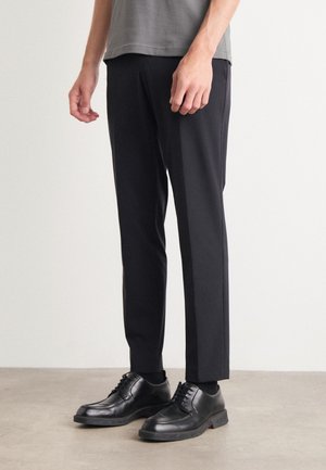 Black tailored trousers made from a lightweight fabric, featuring a straight leg and subtle side pleats. Worn with black lace-up shoes.