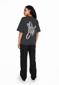 Grå oversized t-shirt med et hvidt grafisk design på ryggen. Stylet med sorte vide bukser og hvide sneakers.