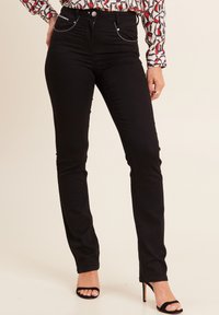 Jeans neri slim-fit con tasche frontali, dettagli in metallo argentato e una texture denim liscia, abbinati a sandali neri con tacco alto.