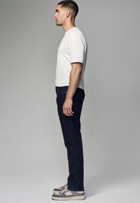 Camiseta blanca de manga corta, jeans azul oscuro y zapatillas gris. Corte ajustado, líneas limpias, diseño minimalista y sin patrones visibles.