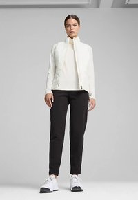 Weiße gesteppte Jacke mit hohem Kragen, kombiniert mit einem cremefarbenen Oberteil, schwarzen Hosen und weißen Sneakers. Gerade Passform und minimalistisches Design.