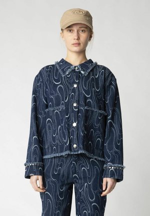 Denim jacket with wave-patterned design, frayed edges, and silver snap buttons. Paired with matching denim pants, featuring decorative accents.