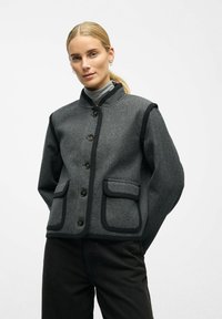 Gray wool blend jacket with a stand collar, button closure, and two front pockets outlined in dark trim. Smooth texture.