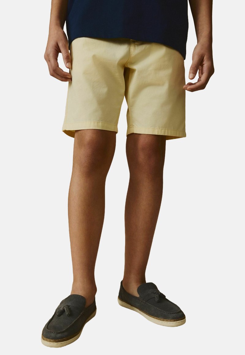Ljust gula bomullsshorts med en avslappnad passform och rak skärning, med sidfickor och klippt fåll. Bärs med mörka slip-on-skor.