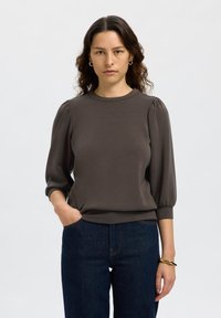 Top fitted di un grigio scuro, con maniche corte a sbuffo e scollatura rotonda. Texture liscia e design semplice, abbinato a jeans blu scuro.