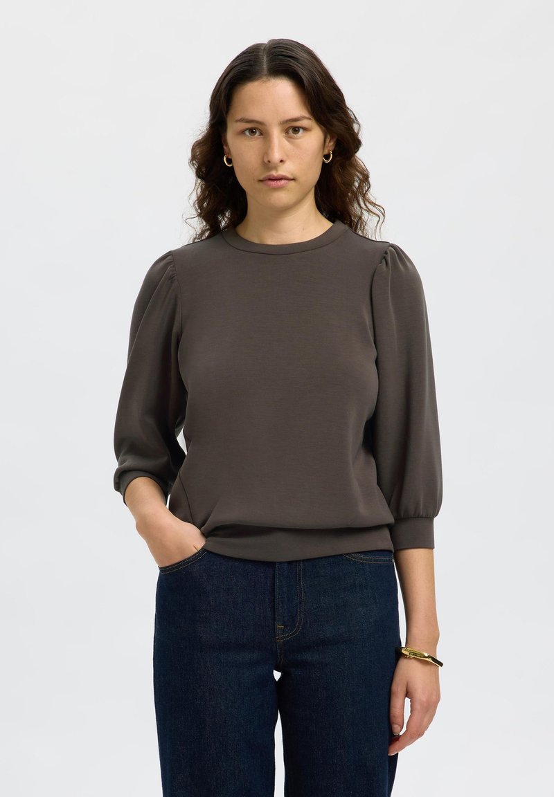 Top fitted di un grigio scuro, con maniche corte a sbuffo e scollatura rotonda. Texture liscia e design semplice, abbinato a jeans blu scuro.
