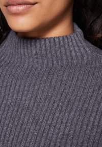Gestrickter Rollkragenpullover in Dunkelgrau; verfügt über vertikale Rippung, weiche Textur und hohen Kragen, der das eng anliegende Design hervorhebt.