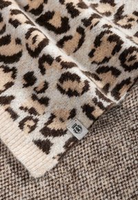 Leopard print wool blanket with a soft texture. Beige and brown color scheme. A small label is visible at the corner, against a houndstooth background.