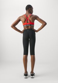 Punane Nike spordirinnahoidja ristatud rihmadega ja must Nike Pro vöökoht, koos mustade põlveni ulatuvate kompressioonipingutustega retuusidega ja mustade sneakeritega.