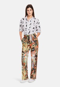 Wit shirt met zwarte abstracte patronen, gecombineerd met kleurrijke, gestreepte broek met een tropisch ontwerp en oranje zijstrepen. Witte sneakers.