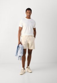 Witte T-shirt met korte mouwen, beige shorts, vastgehouden lichtblauw gestreept shirt. Beige sneakers. Eenvoudige, ontspannen pasvorm. Glad textiel.