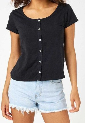 Femme portant une chemise noire à manches courtes avec des boutons, associée à un short en jean bleu clair avec des bords effilochés.