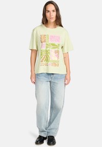 Light green oversized t-shirt featuring a colorful geometric print. Worn with light blue wide-leg jeans and black shoes. Casual fit.