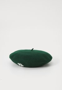 Zeleni filcani beret s zaobljenim oblikom i gornjom petljom. Ima bijeli izvezeni logotip s jedne strane. Glatka tekstura, minimalni dizajn.