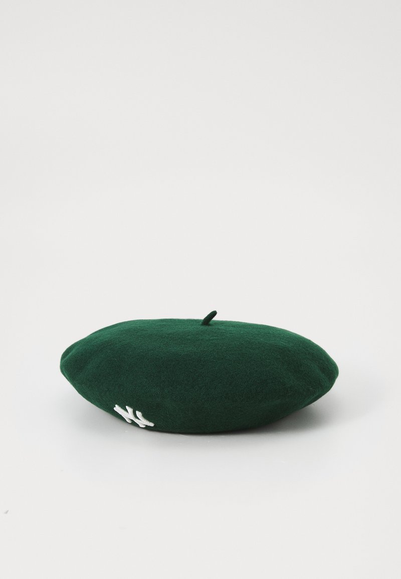 Zeleni filcani beret s zaobljenim oblikom i gornjom petljom. Ima bijeli izvezeni logotip s jedne strane. Glatka tekstura, minimalni dizajn.