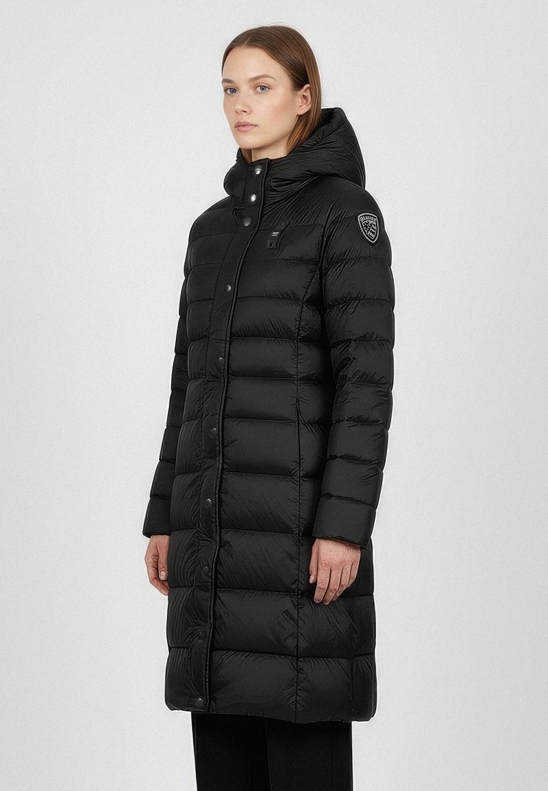 Cappotto lungo nero imbottito con cappuccio, caratterizzato da una texture lucida, chiusura con bottoni e patch del logo sulla spalla sinistra.