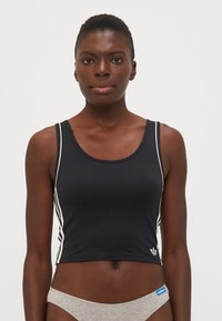 Svart crop top med hvite sidelister, rund halslinje og myk tekstur. Har en liten hvit Adidas-logo ved kanten.