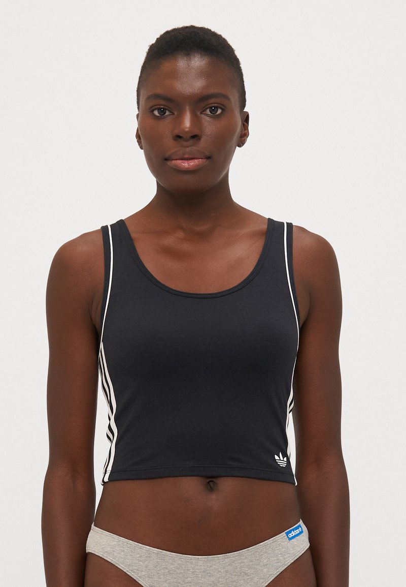 Svart crop top med hvite sidelister, rund halslinje og myk tekstur. Har en liten hvit Adidas-logo ved kanten.