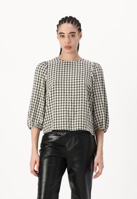 Blusa a quadri gingham bianco e nero con maniche a sbuffo, scollo rotondo e tessuto texture. Abbinata a pantaloni in pelle neri.
