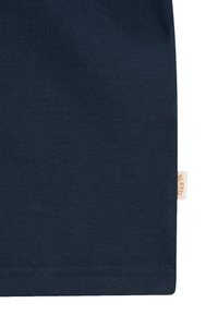 Section de tissu bleu foncé avec une couture visible sur le bord inférieur et une petite étiquette beige avec un texte orange sur le côté droit.