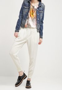 Jeansjacka, blommig t-shirt, krämfärgad tapered byxor och svarta snörskor. Noterbara detaljer inkluderar elastiska manschetter och dragsko i midjan.