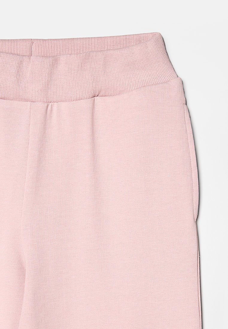 Jasnoróżowe dresy z prążkowanym, elastycznym pasem w talii oraz miękkim, teksturowanym materiałem. Zawierają kieszenie boczne.