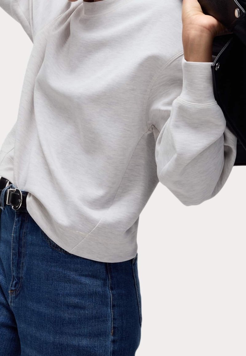 Sweat-shirt gris clair en matière douce, avec coupe décontractée, encolure ronde et poignets côtelés, associé à un jean taille haute bleu foncé.