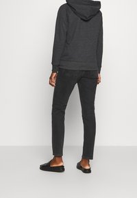 Sudadera gris con capucha y puños acanalados, combinada con jeans oscuros y sandalias negras tipo deslizantes. La vista muestra la parte posterior del atuendo, enfatizando la simplicidad.