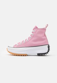 Pink high-top sneaker with canvas upper, white laces, and contrasting rubber sole featuring a black and orange serrated edge.
