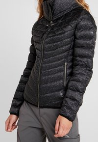 Vadderad svart kviltad jacka med hög krage, texturerad yta, sidofickor med dragkedja och logotyp på nederkanten. Slät tygfinish.