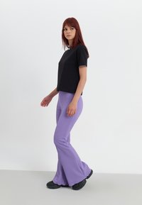 Svart kortermet topp med hvit kant, paret med ribbede lavendel flared bukser og svarte joggesko, mot en hvit bakgrunn.