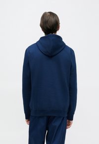 Marineblauwe pullover hoodie gemaakt van een zachte katoenmix, met een capuchon met trekkoord en geribbelde boorden en zoom, gezien vanaf de achterkant.