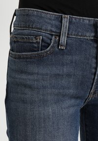 Jeans de mezclilla azul oscuro con un diseño clásico de cinco bolsillos, detalles de costura sutil y una cintura de altura media.