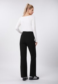 Μαύρο παντελόνι με εφαρμοστή μέση και φαρδιά πόδια, σε συνδυασμό με λευκή μπλούζα μακρυμάνικη. Το σύνολο ολοκληρώνεται με μαύρα παπούτσια με λευκές ρίγες.