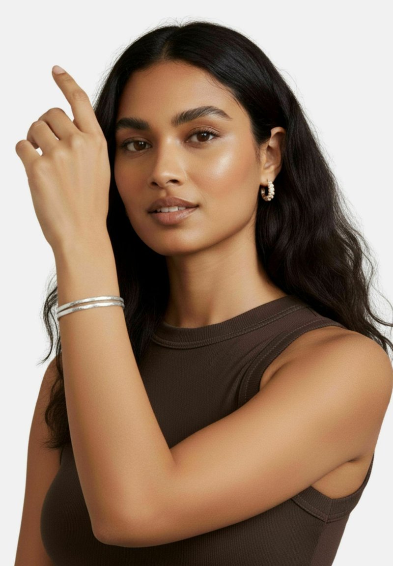 Bracciale a maniche in argento sul polso del modello, con una superficie texturizzata. Il modello ha capelli lunghi e scuri e indossa una maglia senza maniche marrone.