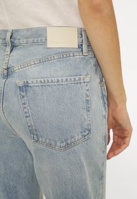 Ljusblå denimjeans med avslappnad passform, med en bakficka, vit läderpatch på midjan och subtila blekningar.