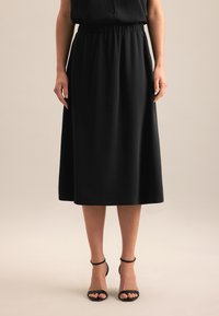 Schwarzer Midi-Rock mit elastischem Bund, glattem Stoff, fließender Silhouette und kombiniert mit schwarzen, geschnürten Absatzsandalen.