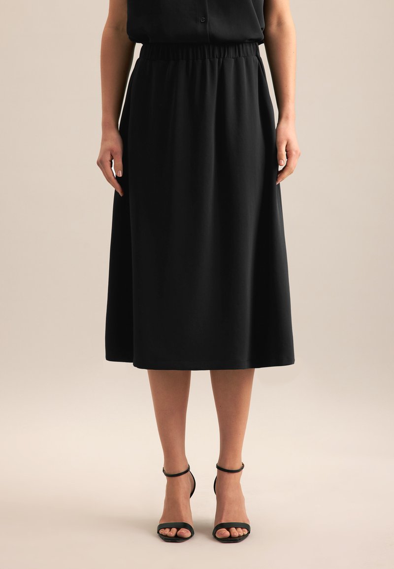 Schwarzer Midi-Rock mit elastischem Bund, glattem Stoff, fließender Silhouette und kombiniert mit schwarzen, geschnürten Absatzsandalen.