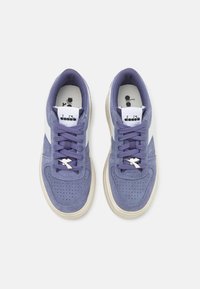 Sneakers in suede viola con accenti bianchi, punta perforata, stringhe piatte viola e suola in gomma color crema. Presentano un'etichetta con il marchio sulla linguetta.
