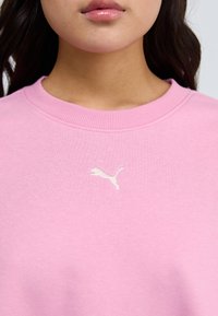 Roze dukserica s rebrastim okruglim izrezom. Ima mali bijeli Puma logo izvezen na prsima. Mekana tekstura.