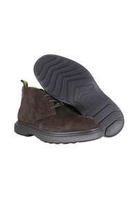 Bruine suède enkellaarzen met grijze rubberen zolen, één laars toont het textuurprofiel van het loopvlak, veters en een gestreepte trekband.