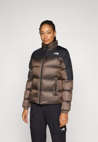 Pufferjack in bruin nylon met zwarte schouderaccenten. Bevat een hoge kraag, ritssluiting en zijzakken voor opbergruimte.