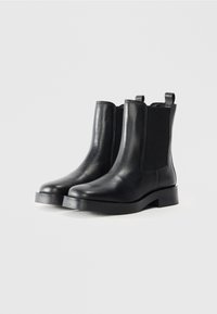 Botas Chelsea de piel negra con paneles elásticos en los laterales, punta redondeada y un tacón bajo. Incluye tiradores para facilitar su colocación.