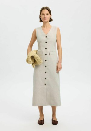 Lys grå linnedress med V-hals, i fuld længde, med frontknapper, sidelommer og et rent, minimalistisk design. Holder en strikket sjal.