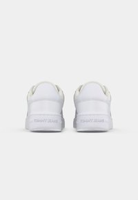 Paire de baskets blanches à semelles épaisses vues de dos, avec "Tommy Jeans" embossé sur le talon de chaque chaussure.