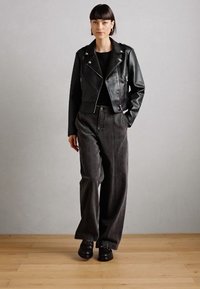 Veste en cuir noire cropped avec des zips argentés, associée à un pantalon large gris foncé et des chaussures à plateforme noires. Texture lisse et design ajusté.