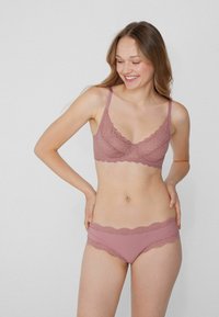 Růžová krajková podprsenka a odpovídající kalhotky s vroubkovanými okraji. Podprsenka má tenké nastavitelné ramínka a měkký strukturovaný design.