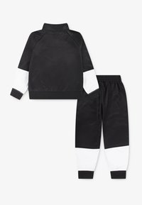 Black athletic tracksuit with white sleeves and cuffs. Silky texture, stand-up collar, elastic waistband. Designed for comfort and movement.