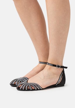 Chaussures plates noires au design ouvert avec des accents en cristal, une sangle à boucle à la cheville et une texture lisse. Élégantes mais pratiques.